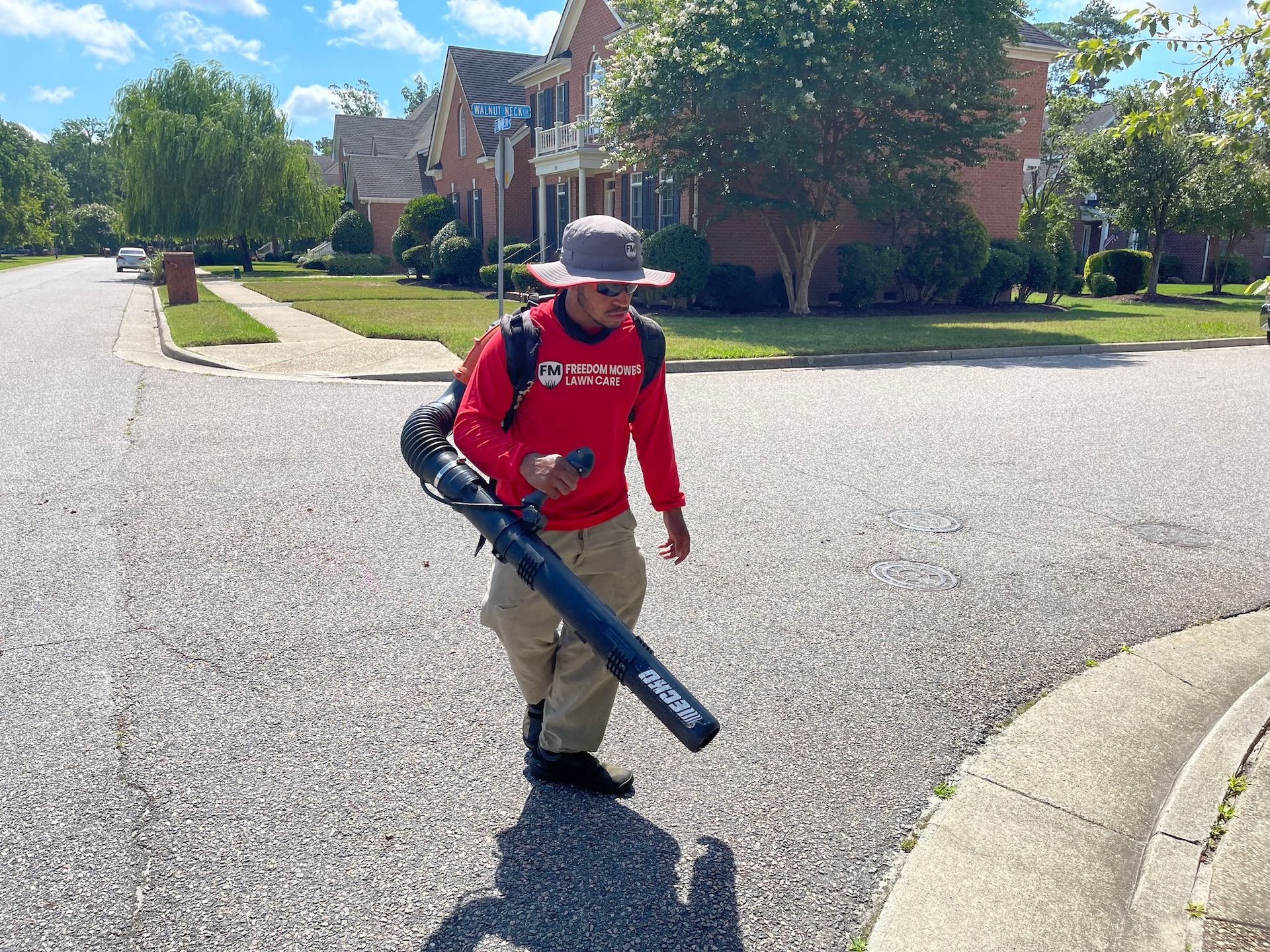 A man is walking down a street with a blower in his hand.