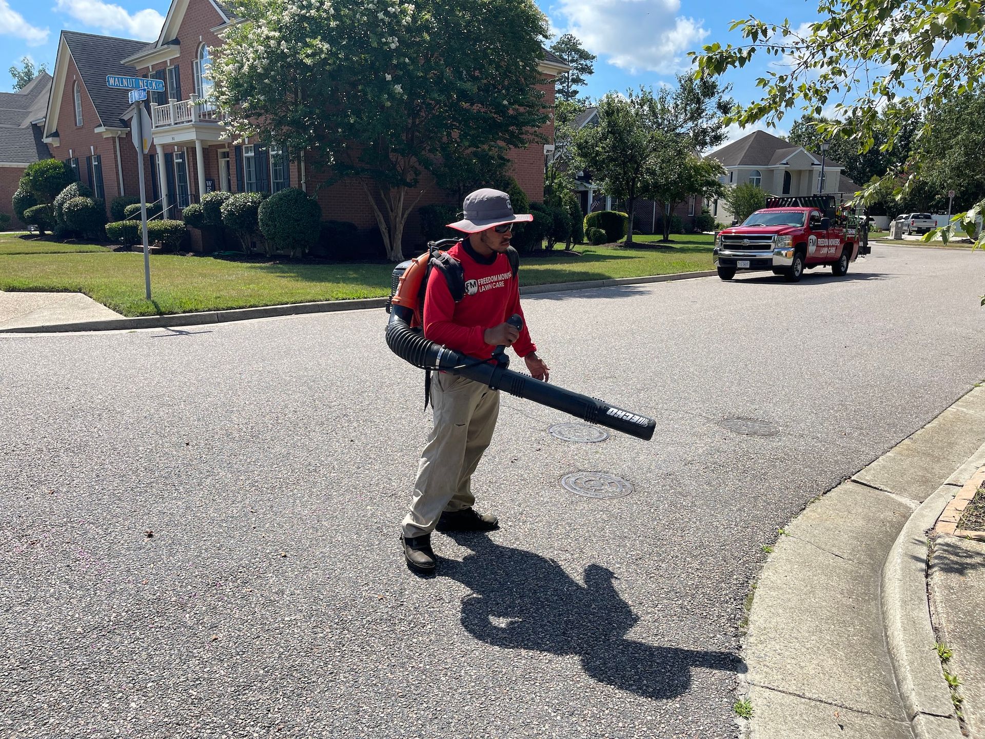 A man is walking down a street with a blower in his hand.