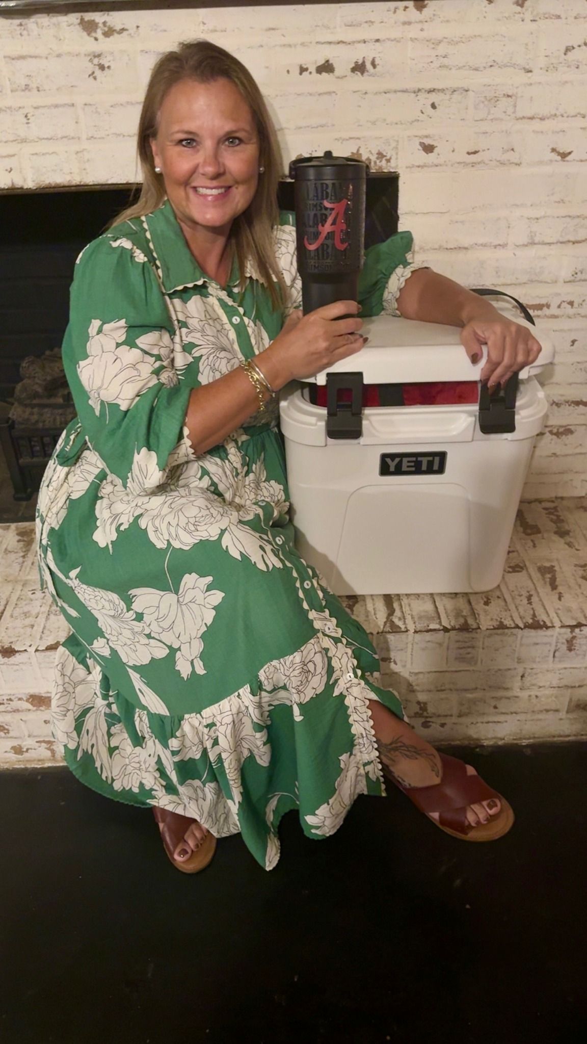 Woman in green dress, holding a large tumbler and sitting next to a white Yeti cooler.