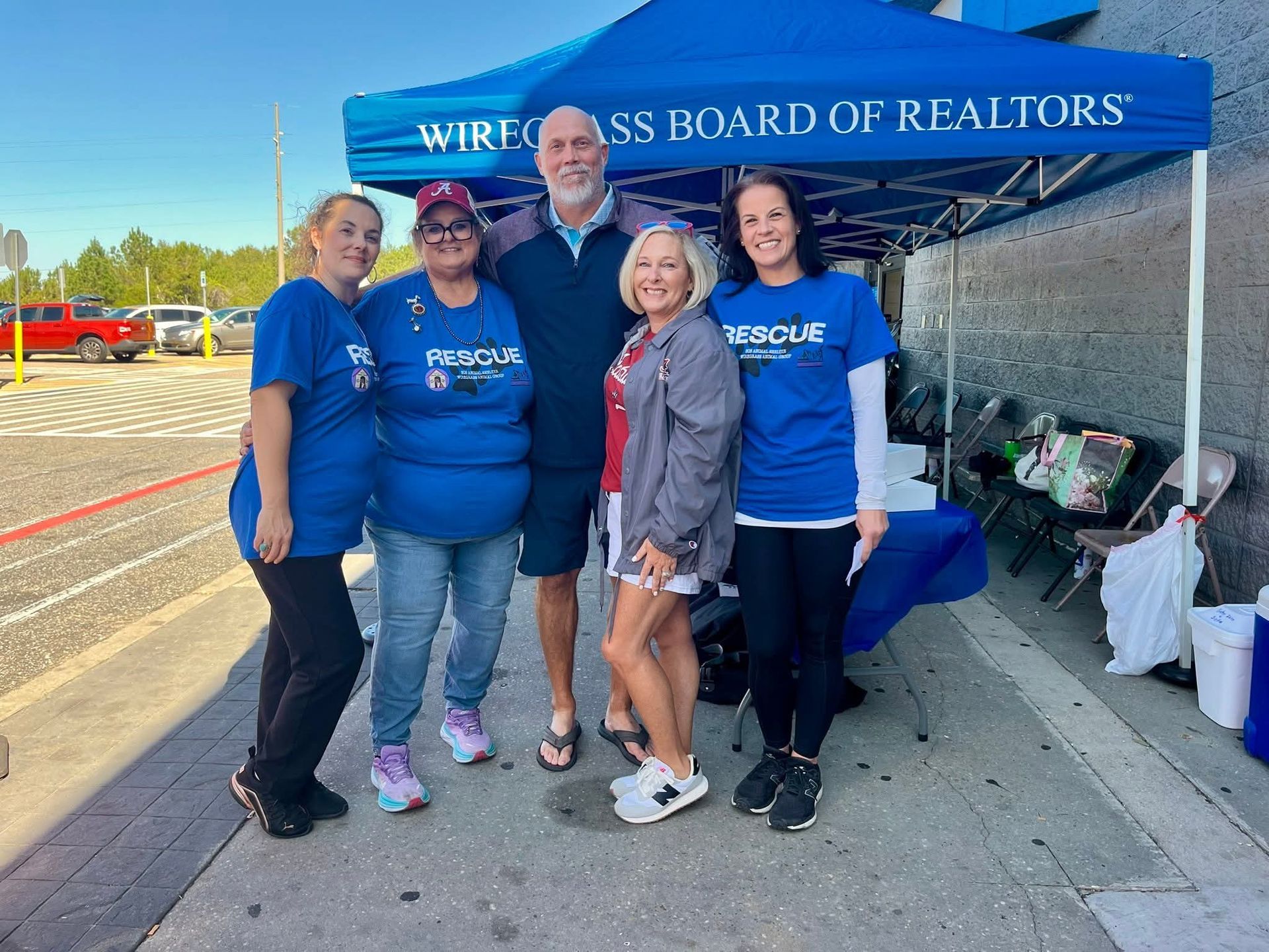 People in blue shirts and a grey-haired man pose under a Realtors tent.
