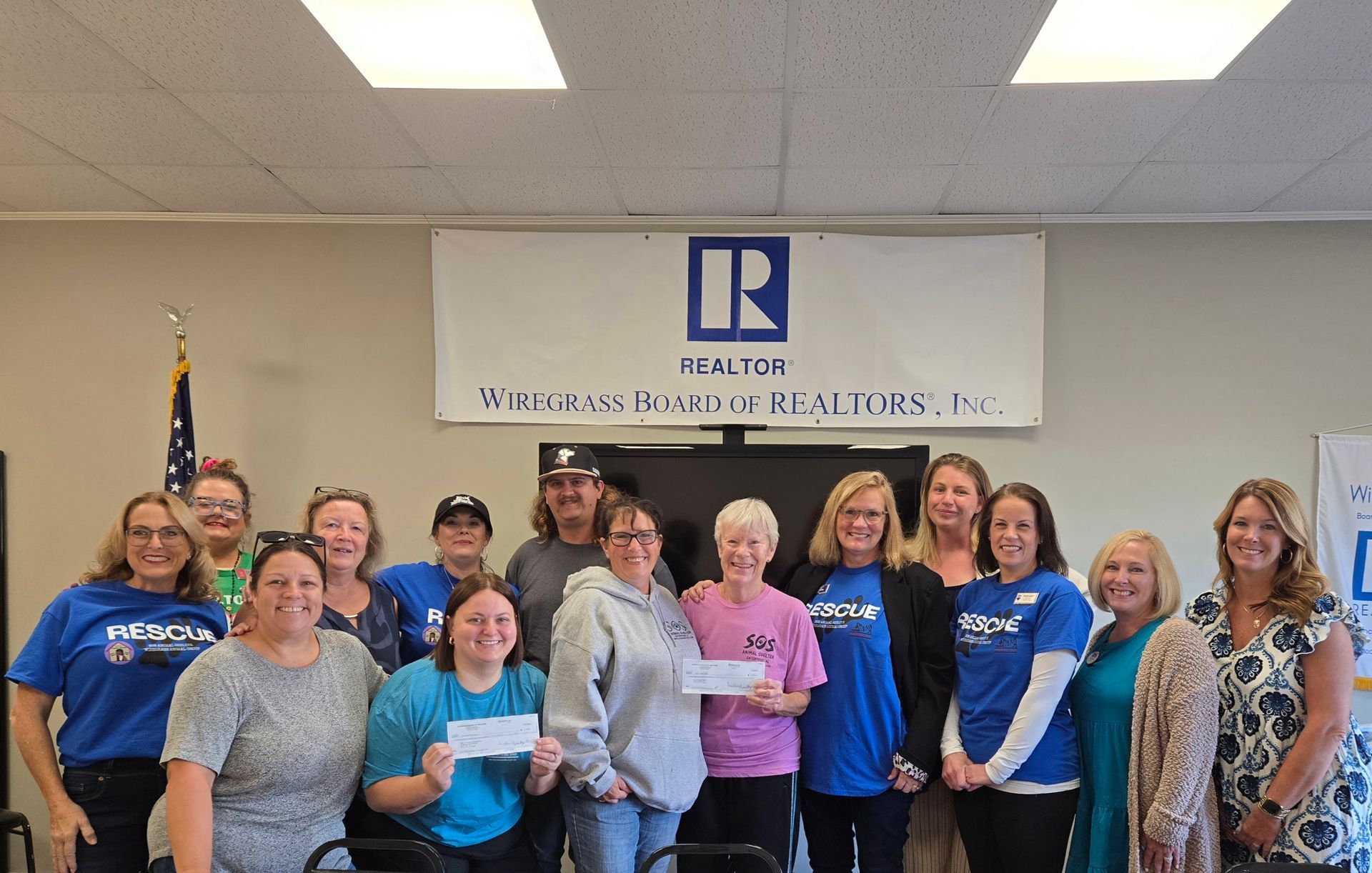 Group of people holding a check in an office, likely a donation presentation. 