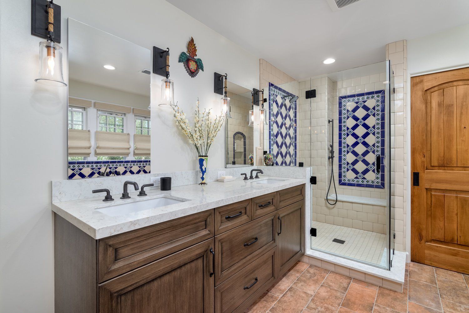 Bathroom with double vanity, large mirror, and glass shower with blue tile accents