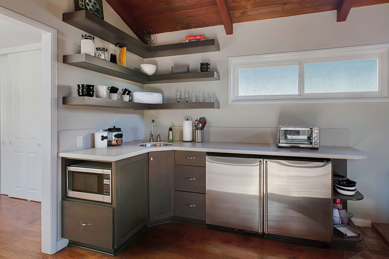 Modern kitchen with stainless-steel appliances, open shelves, and white counters under a wood-beamed ceiling