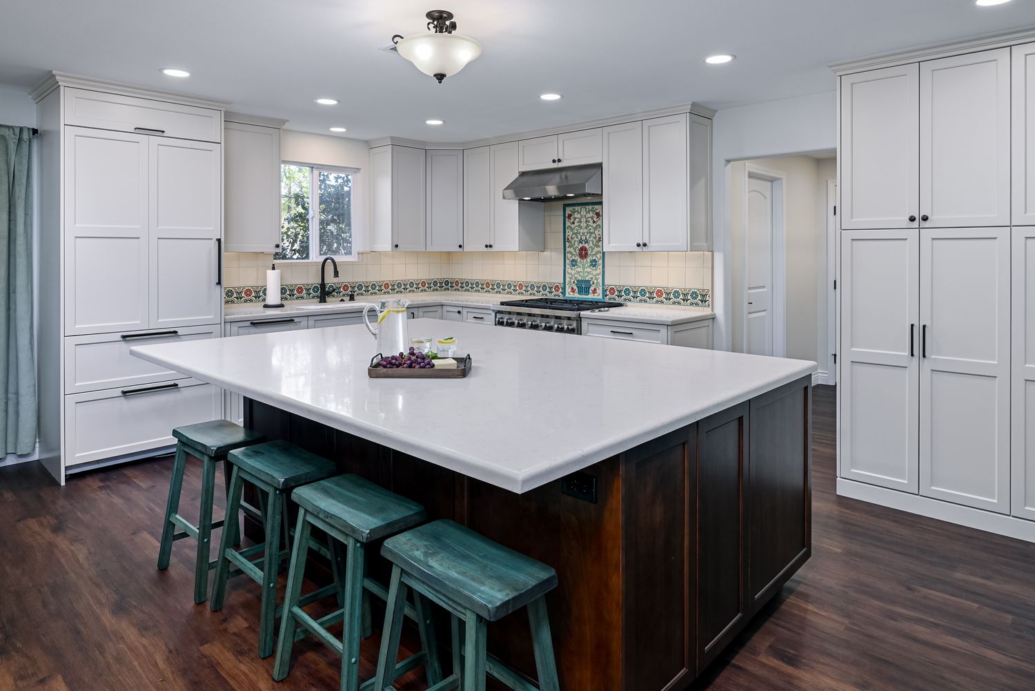 Bright modern kitchen with a large island, teal stools, white cabinets, and dark wood floors