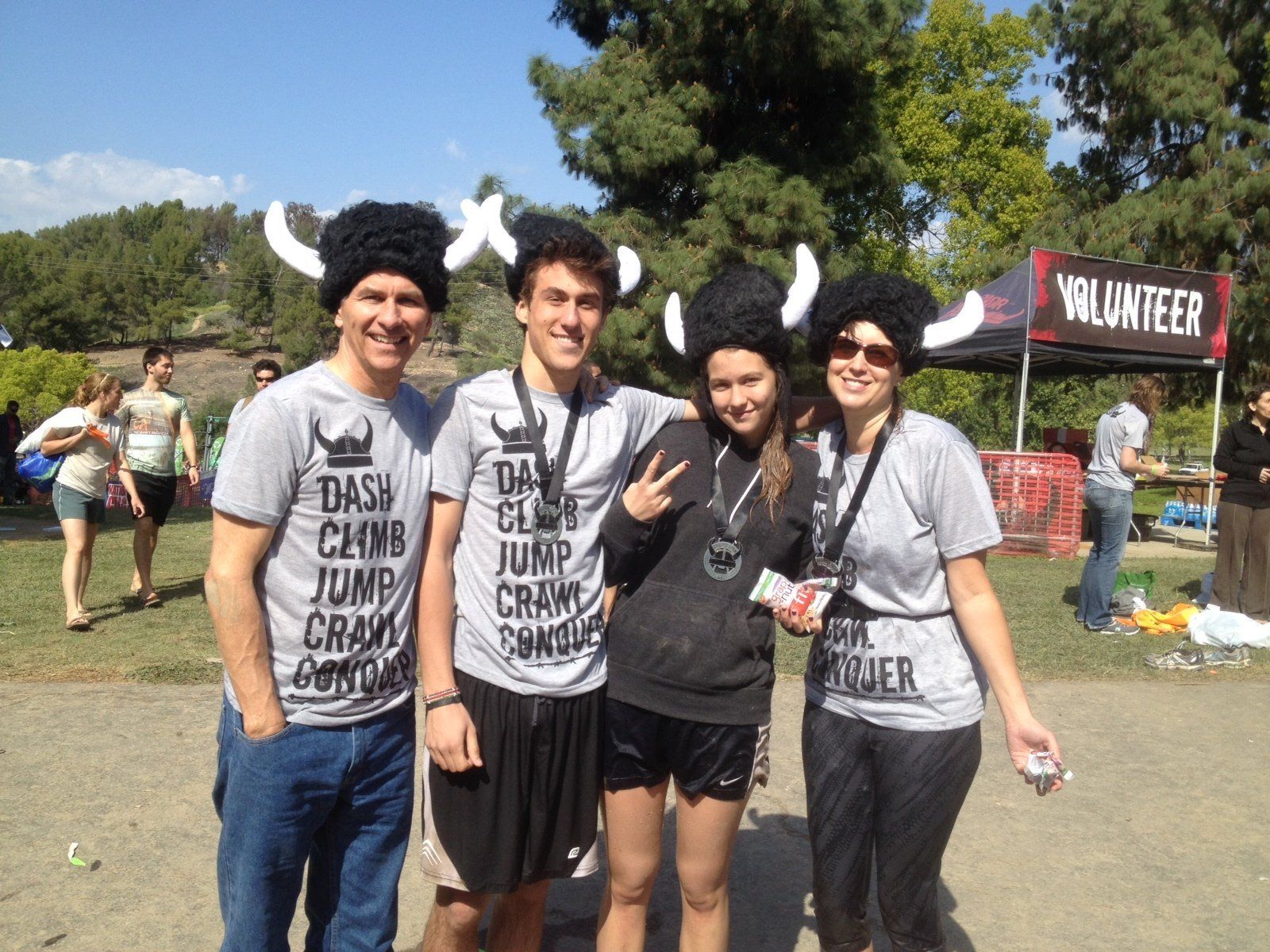 Four volunteers in horned hats pose outdoors at a charity event near a “Volunteer” tent.