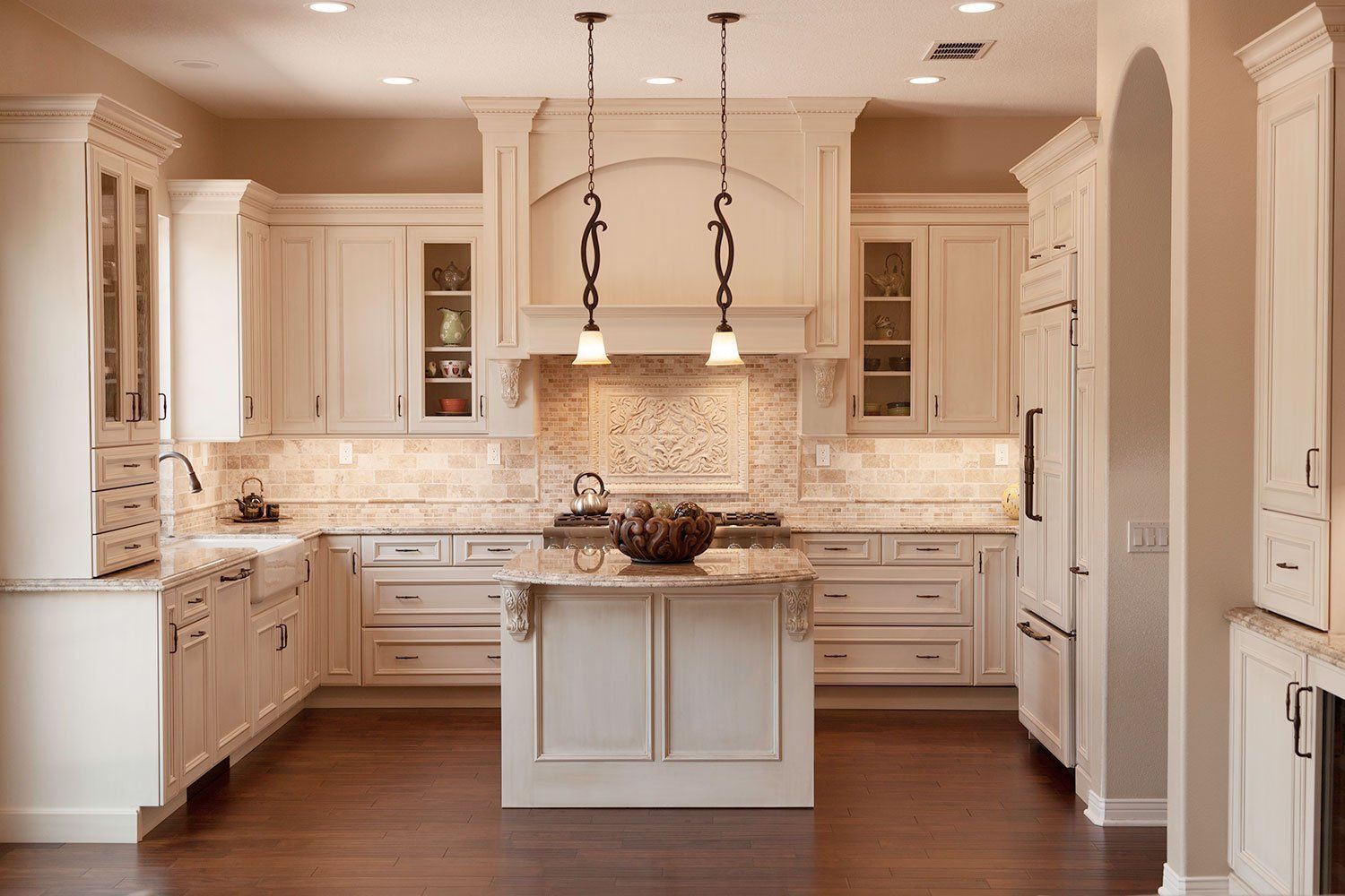 Bright white kitchen with marble countertops, island, pendant lights, and dark hardwood floors