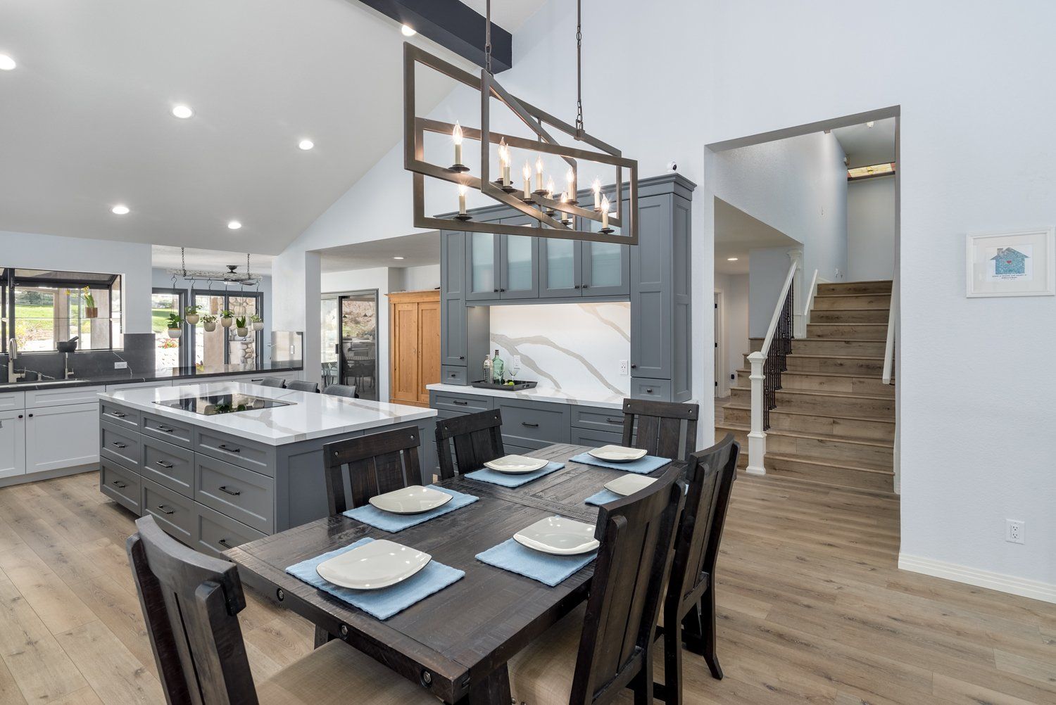 Modern open kitchen and dining area with island, black table, and staircase in the background