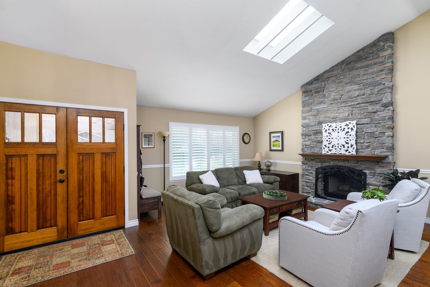Bright living room with green and white sofas, stone fireplace, wood floor, and large wooden cabinet