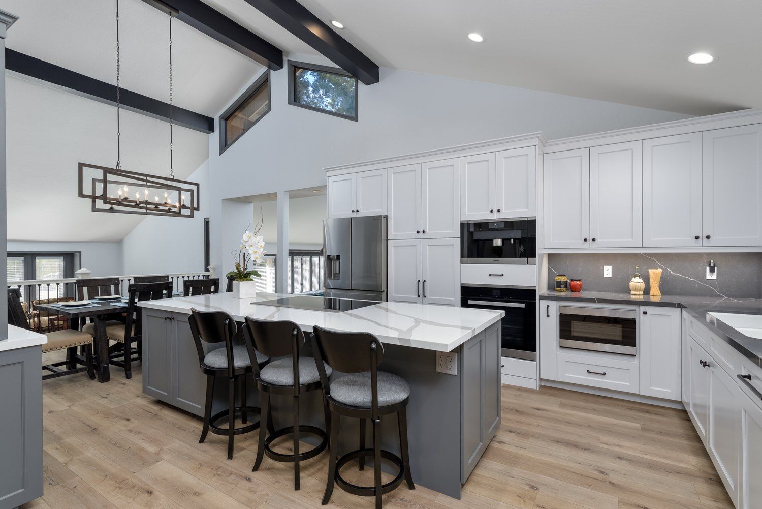 Modern kitchen with large black island, wooden cabinets, pendant lights, and bar stools