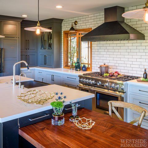 Bright kitchen with blue cabinets, white island, black range hood, and wooden dining table.