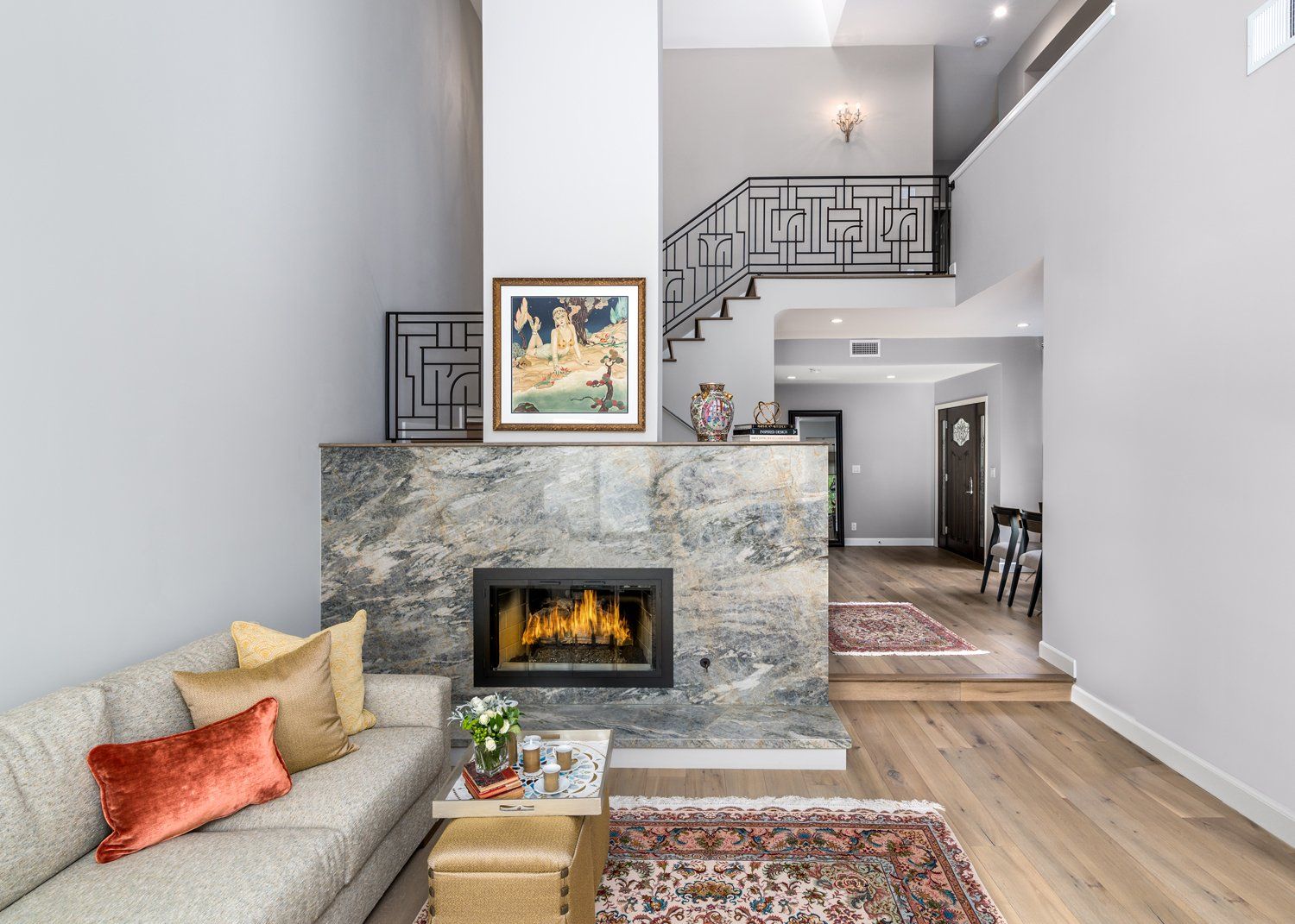 Modern living room with stone fireplace, gray sofa, colorful pillows, and staircase in background