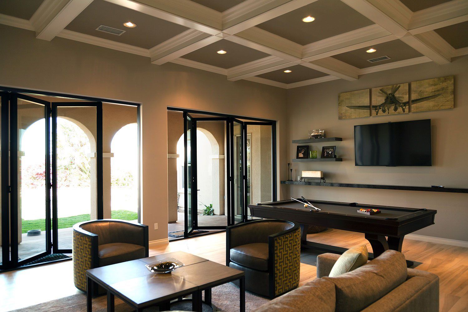 Modern living room with sectional sofa, pool table, wall-mounted TV, and large glass doors