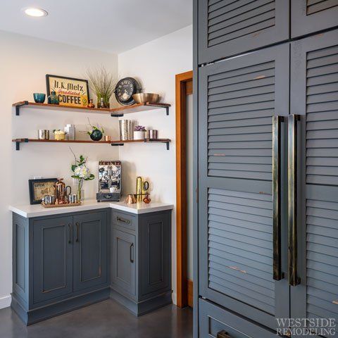 Built-in corner coffee bar with gray cabinets, wood shelves, and decor beside a louvered pantry door