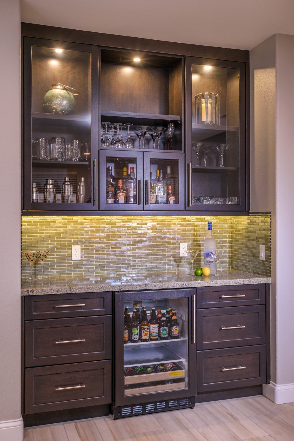 Dark wood bar cabinet with glass shelves, wine cooler, and mosaic tile backsplash in a home interior