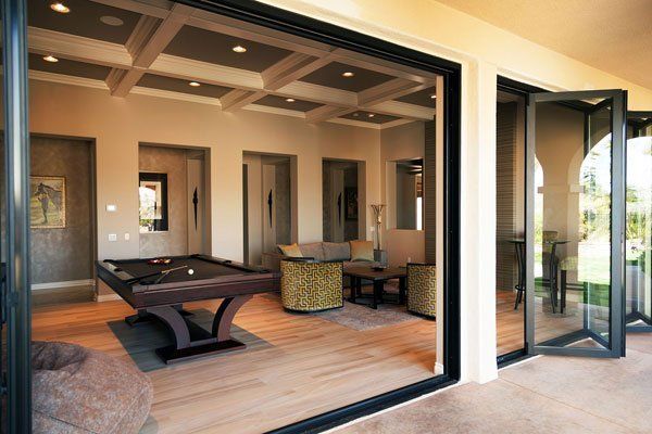 Open patio doors to a modern lounge with pool table, wicker chairs, and wood floors