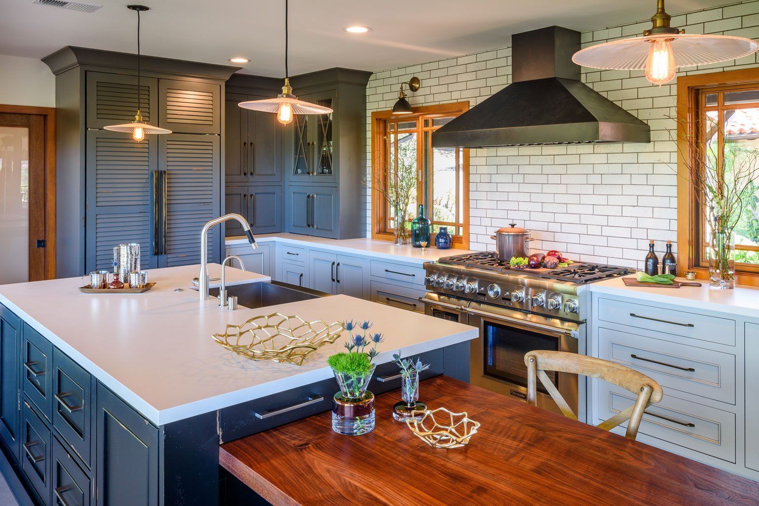 Modern kitchen with large island, dark cabinets, white tile backsplash, and wood dining table by the window