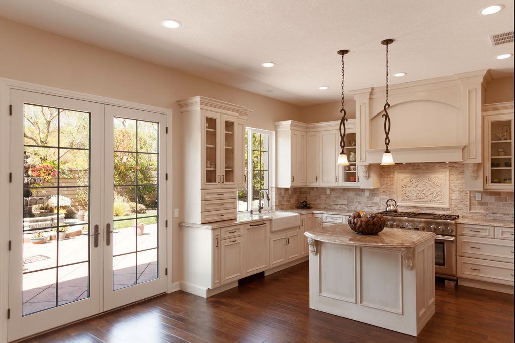 Bright modern kitchen with white cabinets, stone backsplash, island, and French doors to a patio.