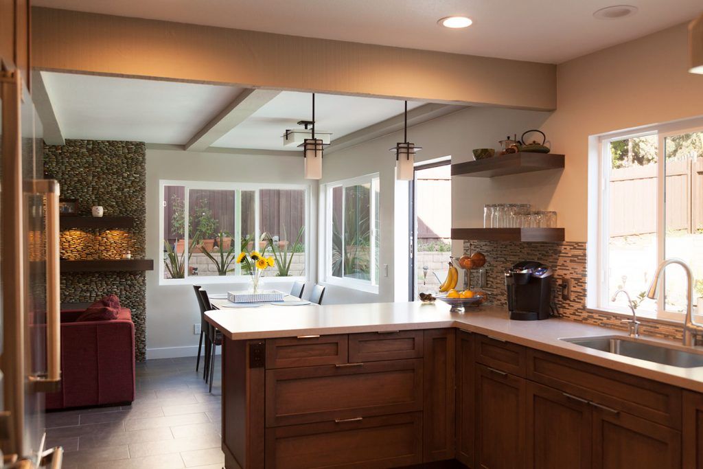 Modern kitchen with wood cabinets, white countertops, dining area, and large windows overlooking a patio.