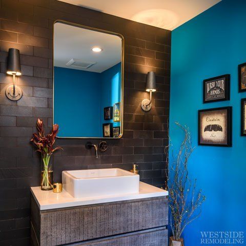 Modern bathroom vanity with white sink, black tile wall, turquoise accent wall, and framed art.