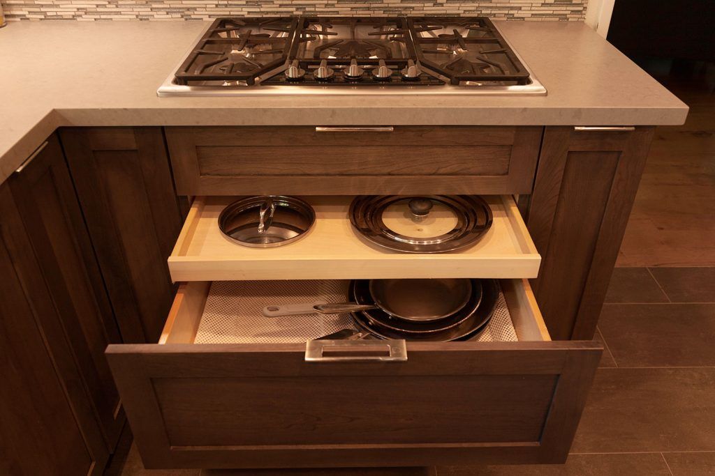 Built-in kitchen cabinet drawer with pull-out shelves holding pots and pans under a cooktop