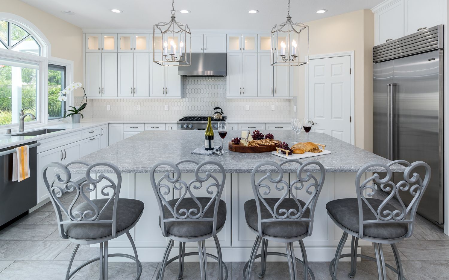 Bright white kitchen with island, barstools, chandelier, and stainless steel appliances.