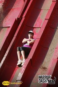 Person sitting on a red obstacle course ramp, holding arms crossed, with a helmet on.