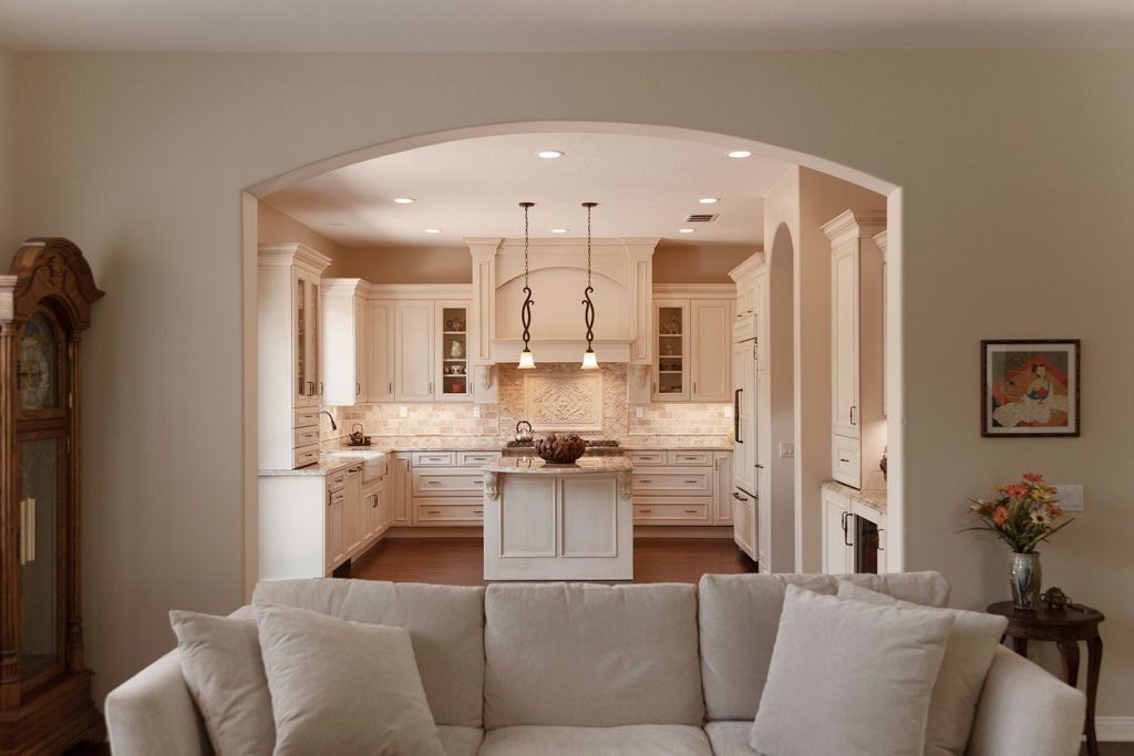 Living room with beige sofa facing an arched opening to a bright white kitchen
