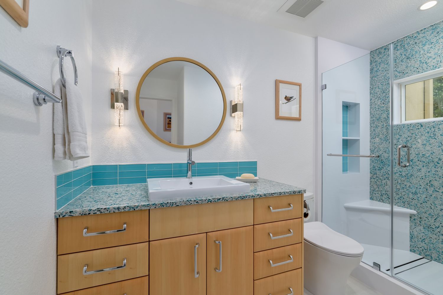 Modern bathroom with wood vanity, round mirror, turquoise backsplash, and glass shower stall