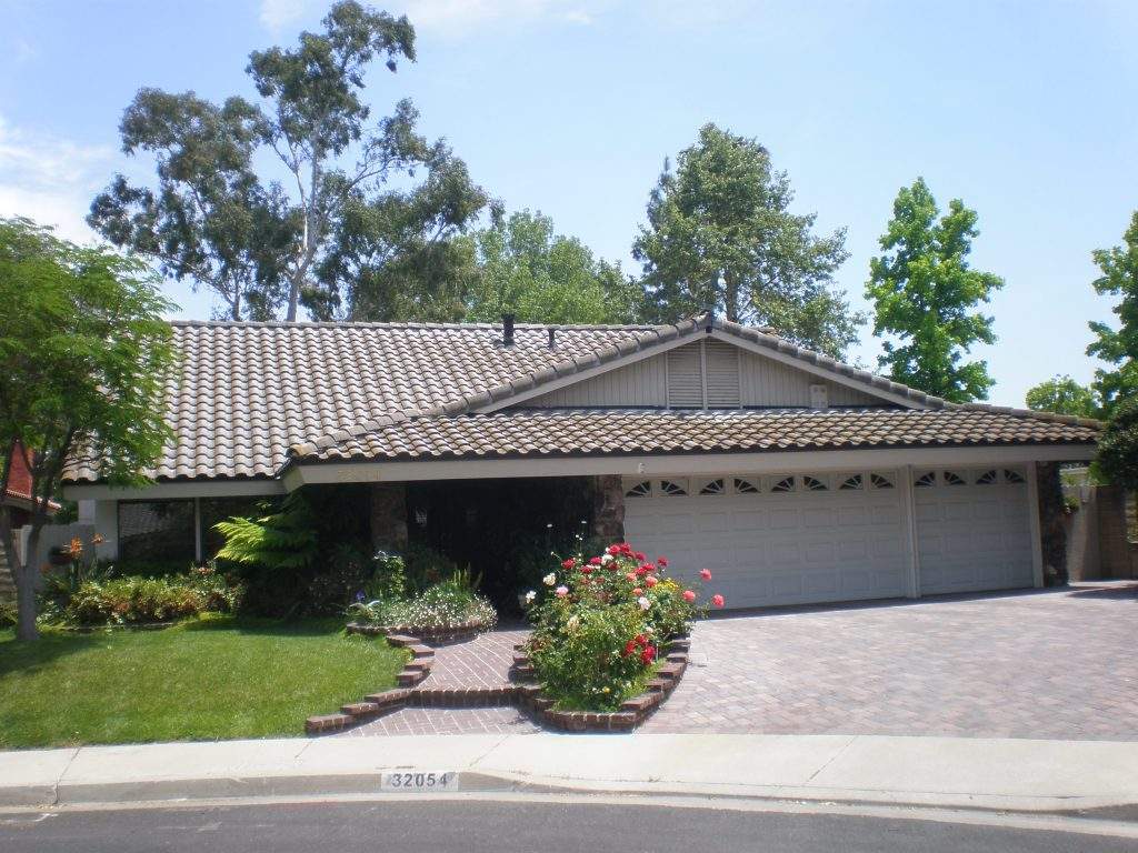 Single-story suburban house with tiled roof, two-car garage, and front garden under a blue sky