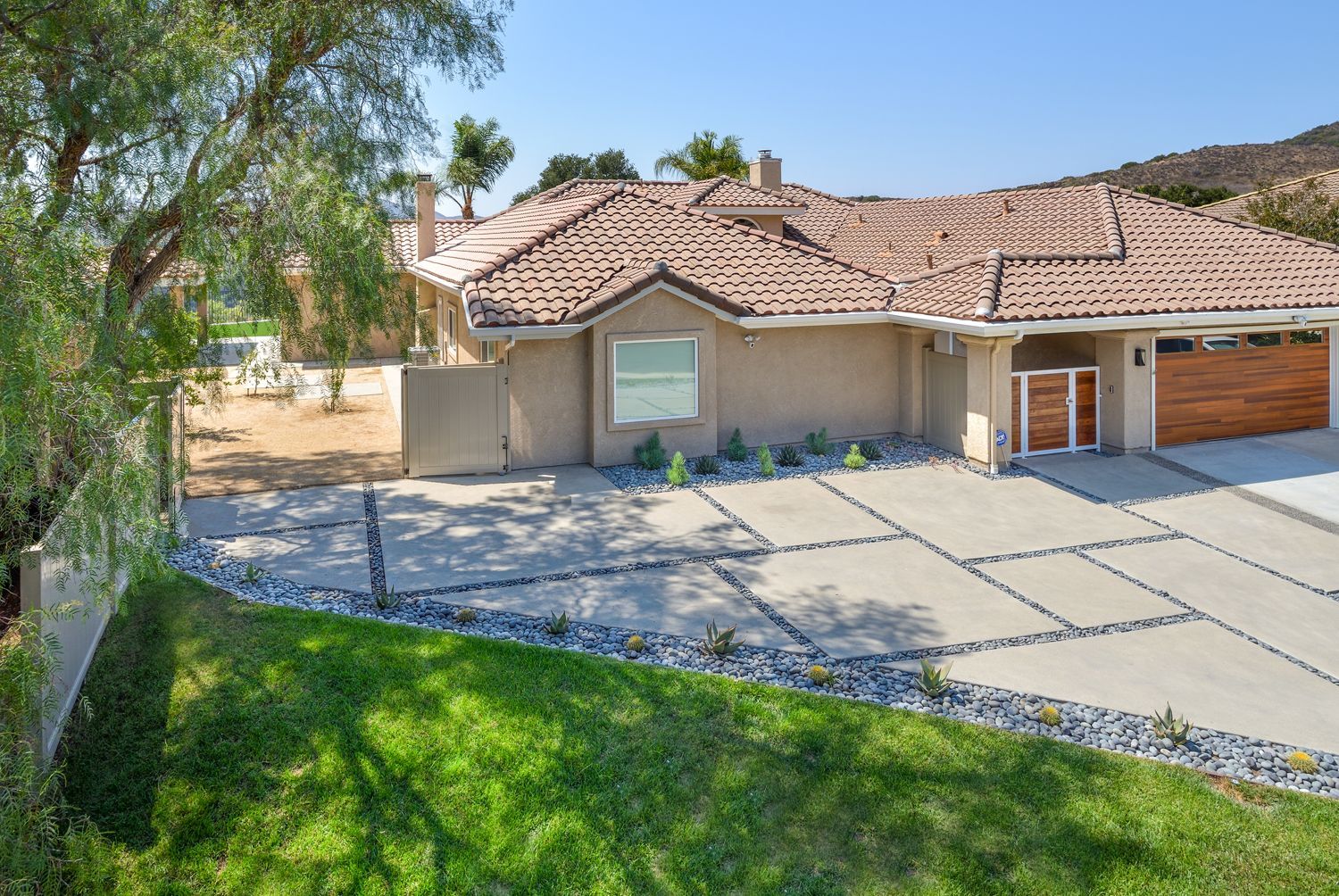 Suburban house with tiled roof, wide driveway, and green lawn under a clear blue sky
