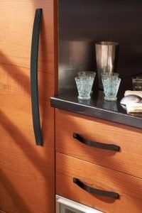 Wooden kitchen cabinet with black curved handles and countertop glasses and a metal tumbler
