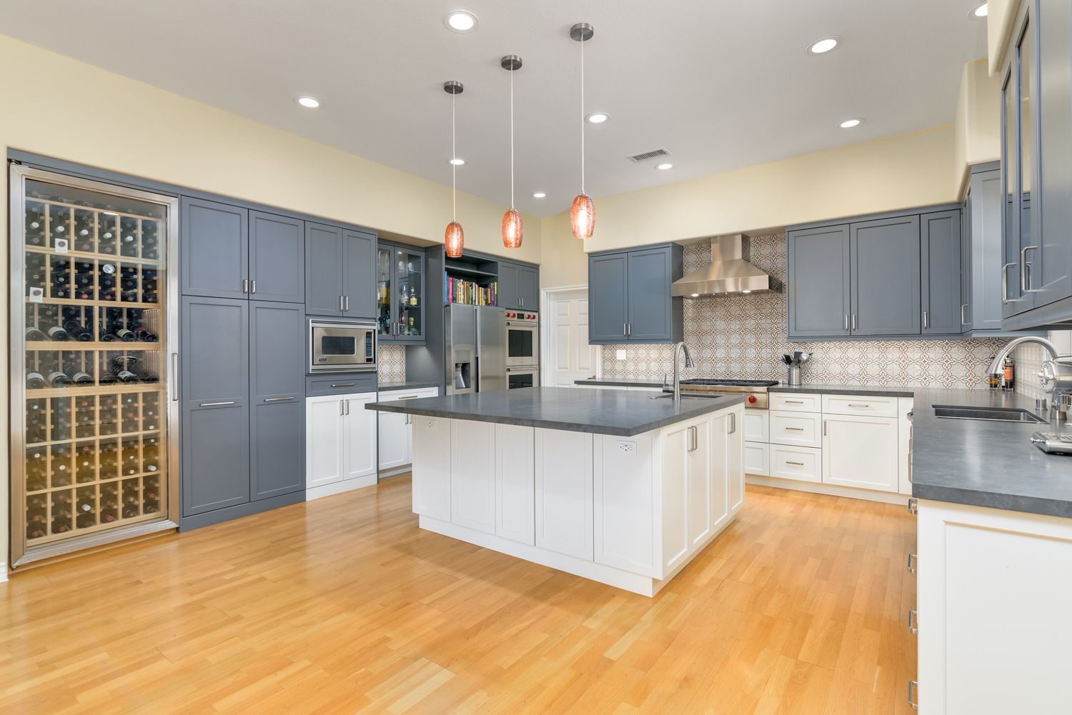 Modern kitchen with blue-gray cabinets, white island, stainless appliances, and hardwood floors