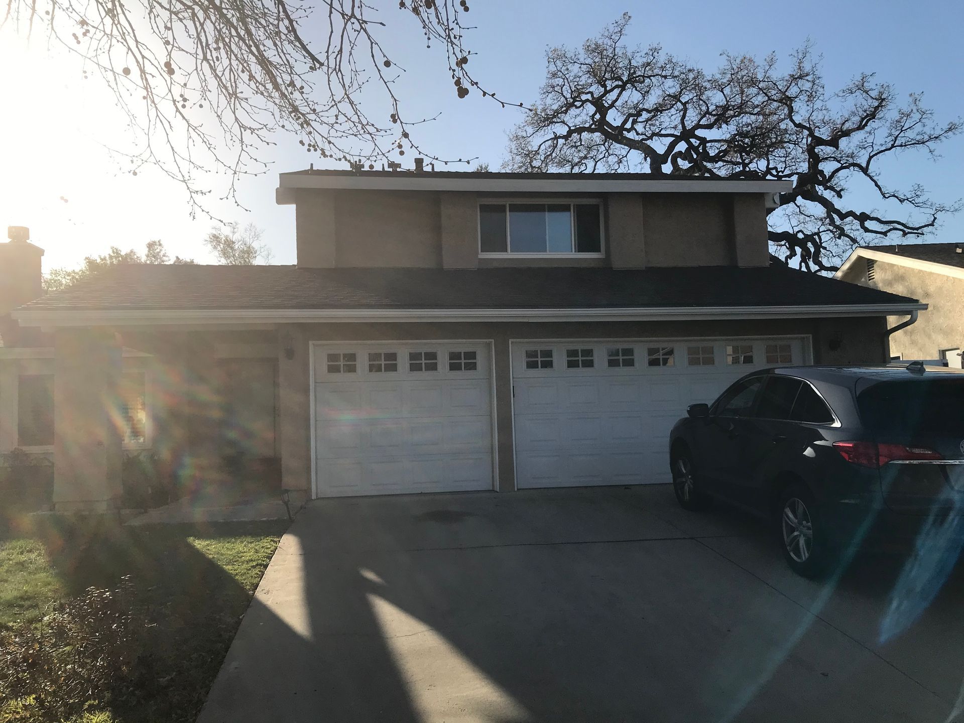 Suburban two-story house with a double garage and a black SUV in the driveway at sunset.