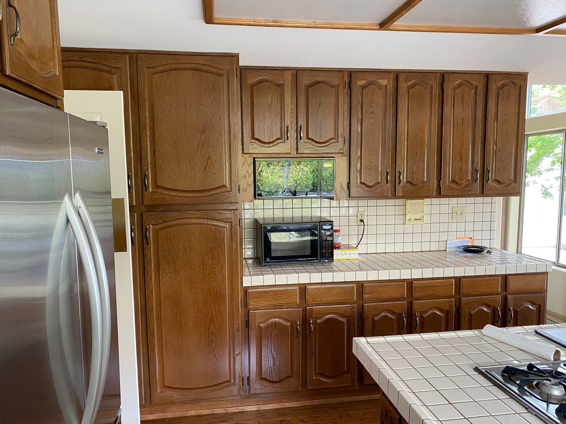 Small kitchen with wood cabinets, white tile backsplash, stainless fridge, and a stove in the foreground