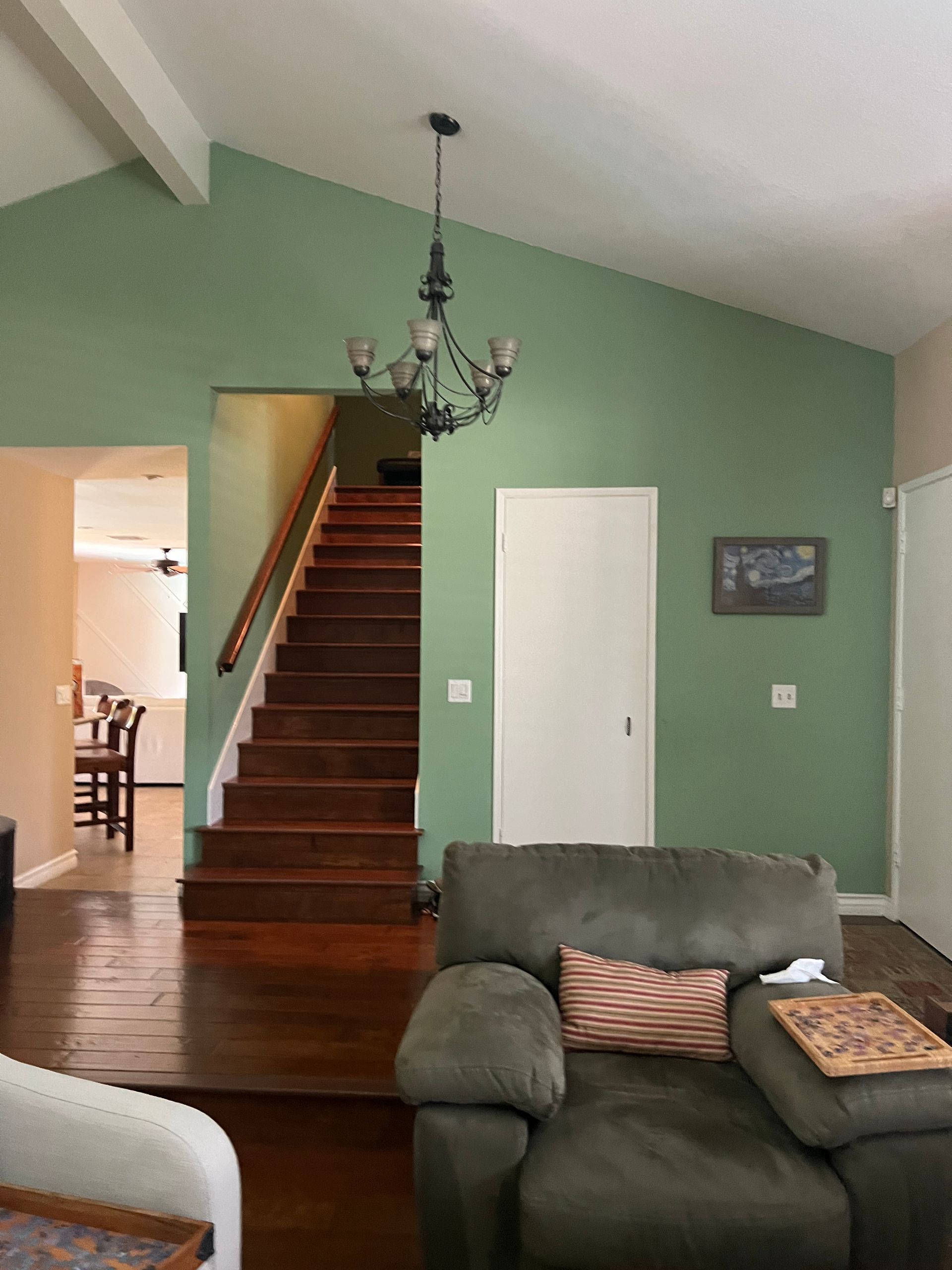 Living room with green walls, staircase, chandelier, and dark green couch