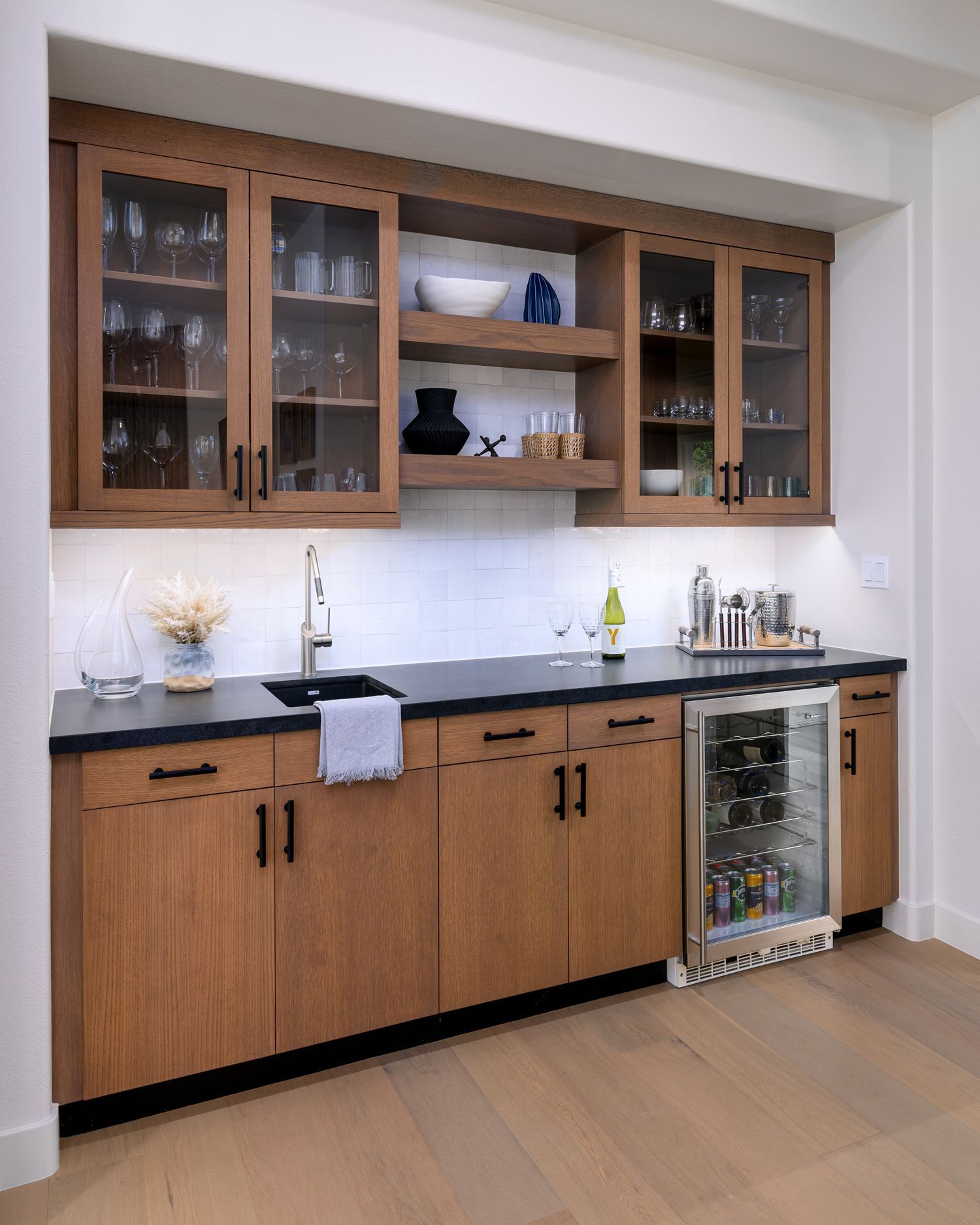 Built-in kitchen cabinet with wooden doors, glass-front shelves, black countertop, and under-counter wine cooler.