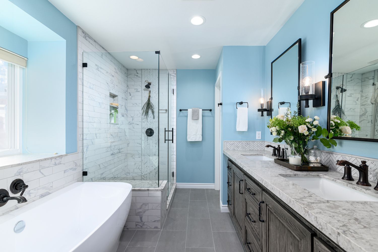 Bright modern bathroom with freestanding tub, glass shower, double vanity, and light blue accents