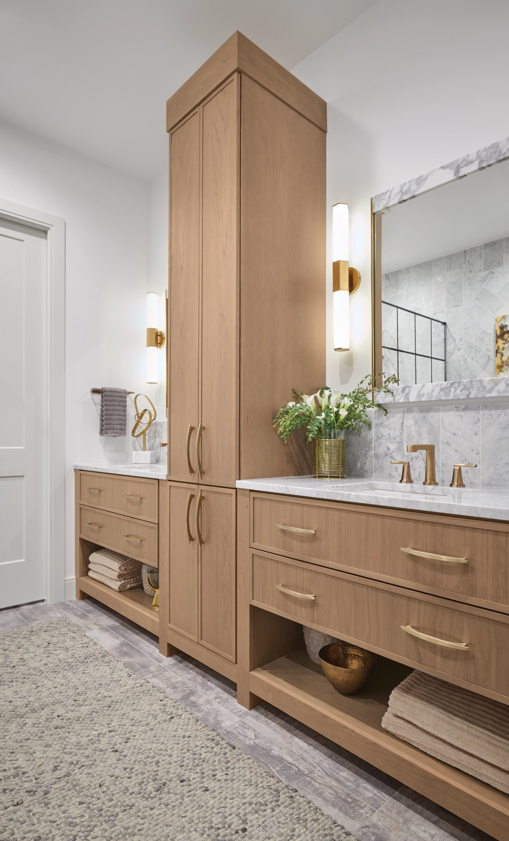 Modern bathroom with wood vanity, tall storage cabinet, mirror, and gold wall sconces