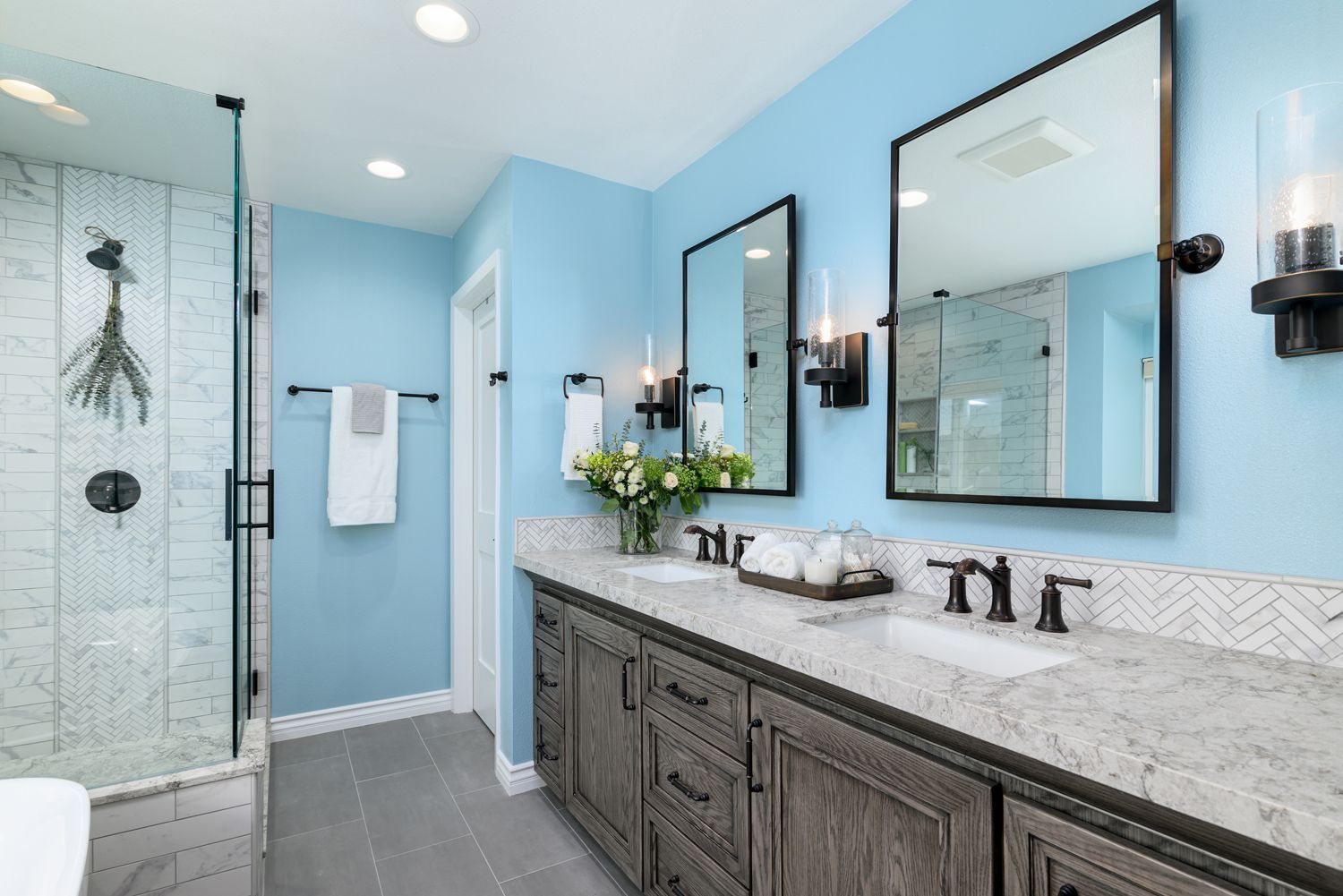 Bright bathroom with glass shower, blue walls, and dark wood vanity with mirrors.