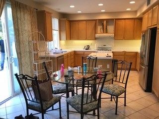 Bright kitchen with wooden cabinets and a glass table with four chairs on a tiled floor.