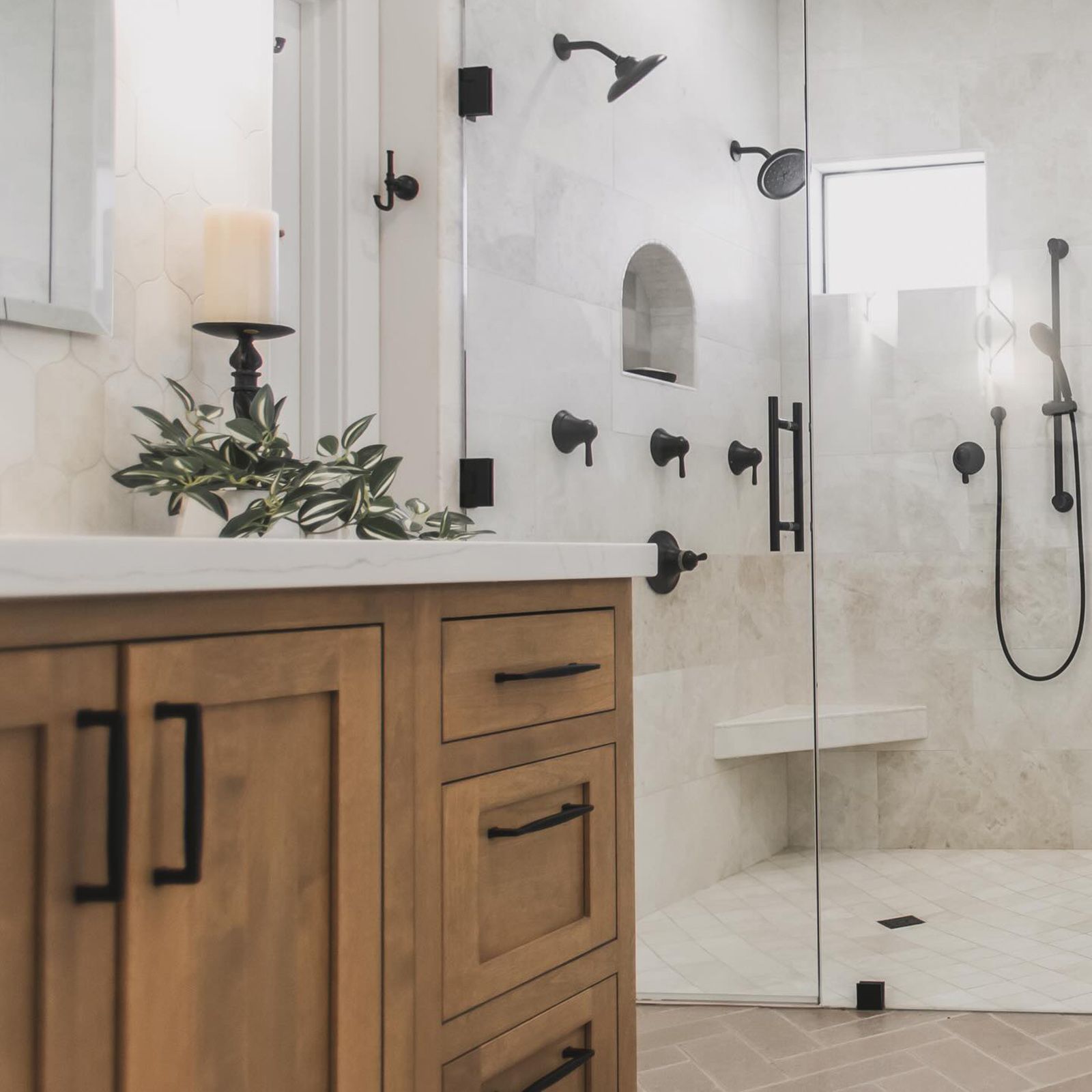 Modern bathroom with wood vanity, white marble walls, black fixtures, and glass shower.