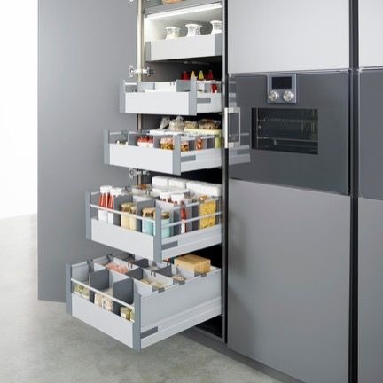 Open kitchen pantry drawers filled with food, next to a stainless steel refrigerator and oven.