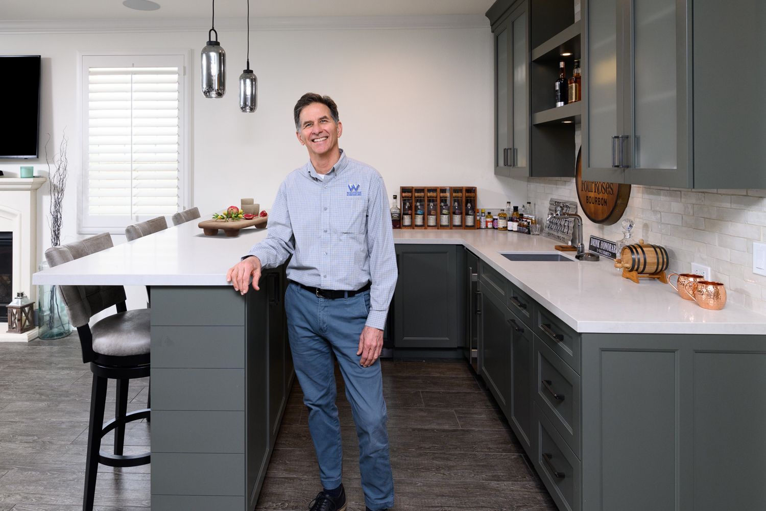 Man standing in a modern kitchen beside a white island, smiling with hands on the counter.