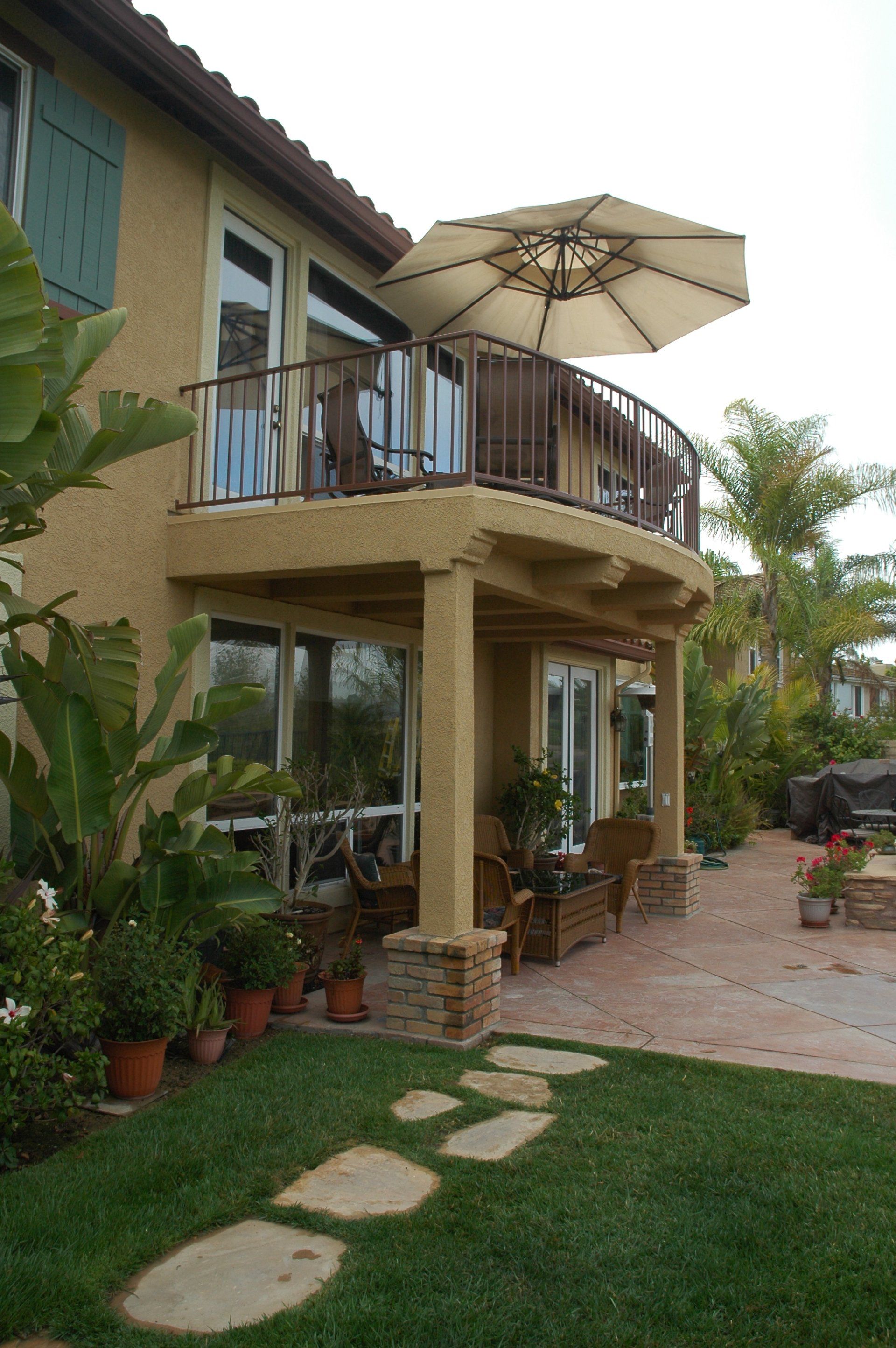 Two-story house with balcony, patio umbrella, and potted plants beside a green lawn