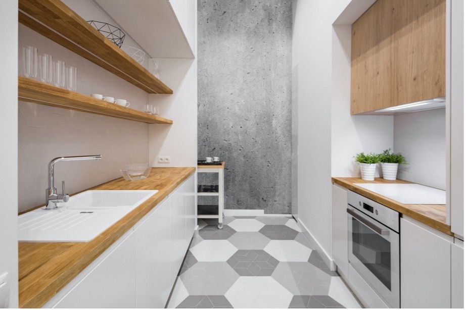 Modern narrow kitchen with white cabinets, wooden shelves, gray counter, and hexagon tile floor.