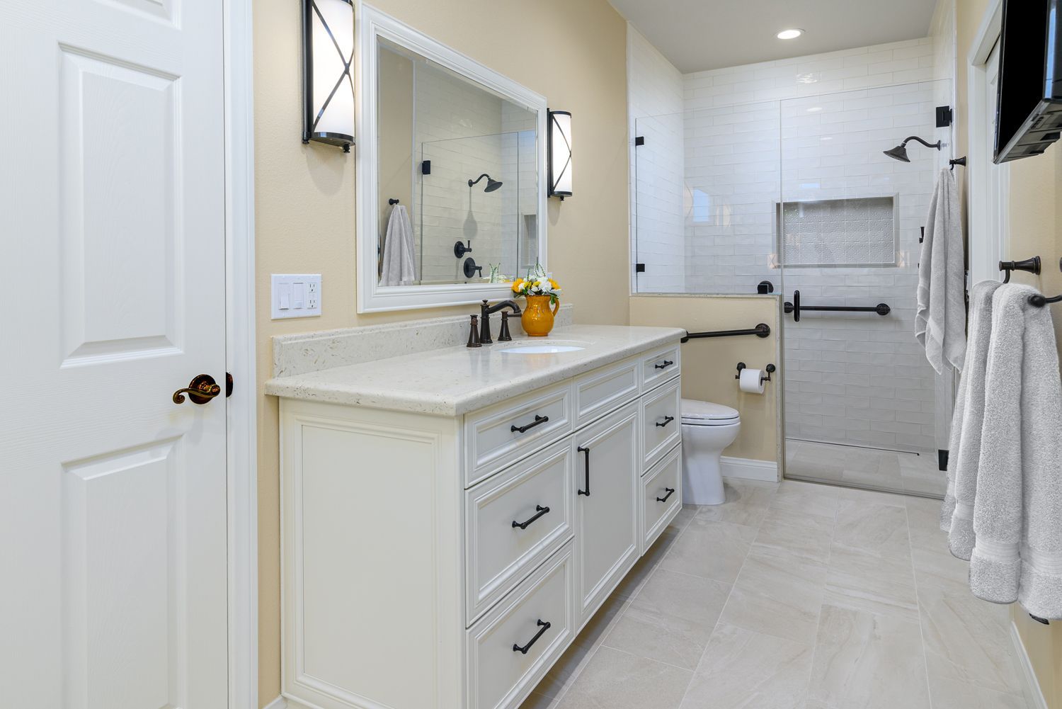 Bright bathroom with cream vanity, large mirror, toilet, and glass shower door, in a clean neutral design
