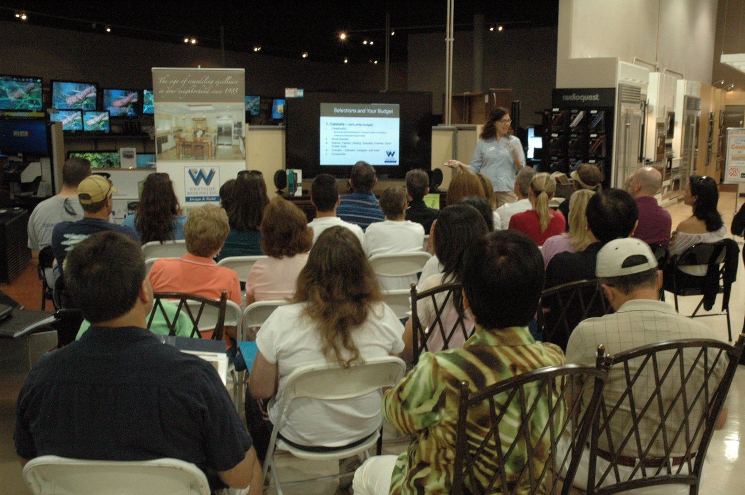 Audience seated in a mall listening to a presentation on a screen at the front