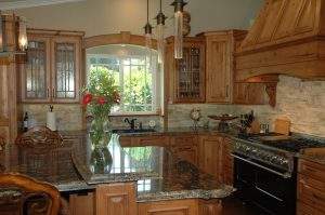 Wooden kitchen with granite island, black stove, and a bright window above the sink