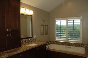 Bathroom vanity with dark wood cabinets, granite countertop, mirror, and a window above the sink.