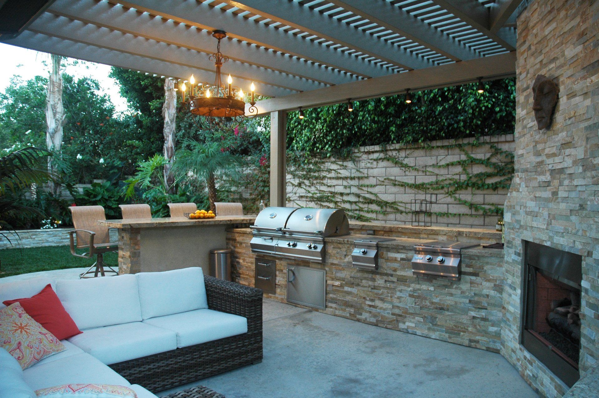 Outdoor patio with stone grill, wicker sofa, bar stools, and pergola lighting